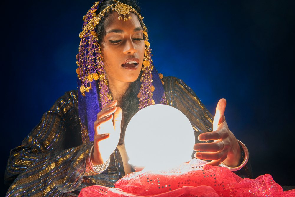 A woman dressed as a fortune teller uses a glowing crystal ball in a mystical setting in the, USA.