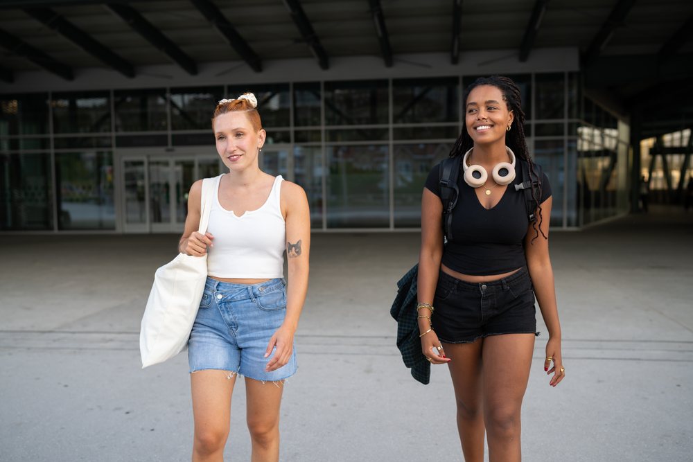 Two young women walk side by side in casual summer clothes outside a modern building, urban, Santiago De Compostela, Spain.