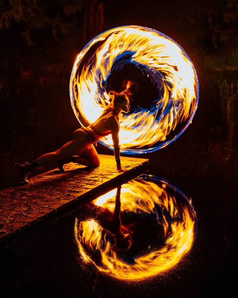 Fire dancer spins flames on a pier at night with reflections in the water, artistry, artist, USA.