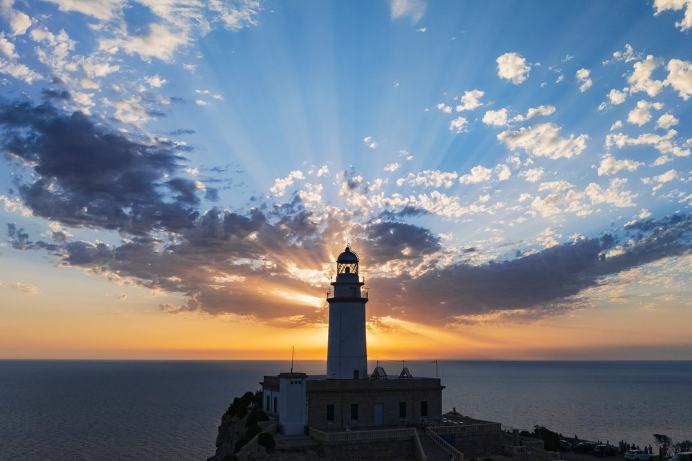 Lighthouse at Cap de Formentor on Mallorca silhouetted against sunrise with sun rays through clouds over the sea, Landscape, Lifestyle, Polença, Spain.