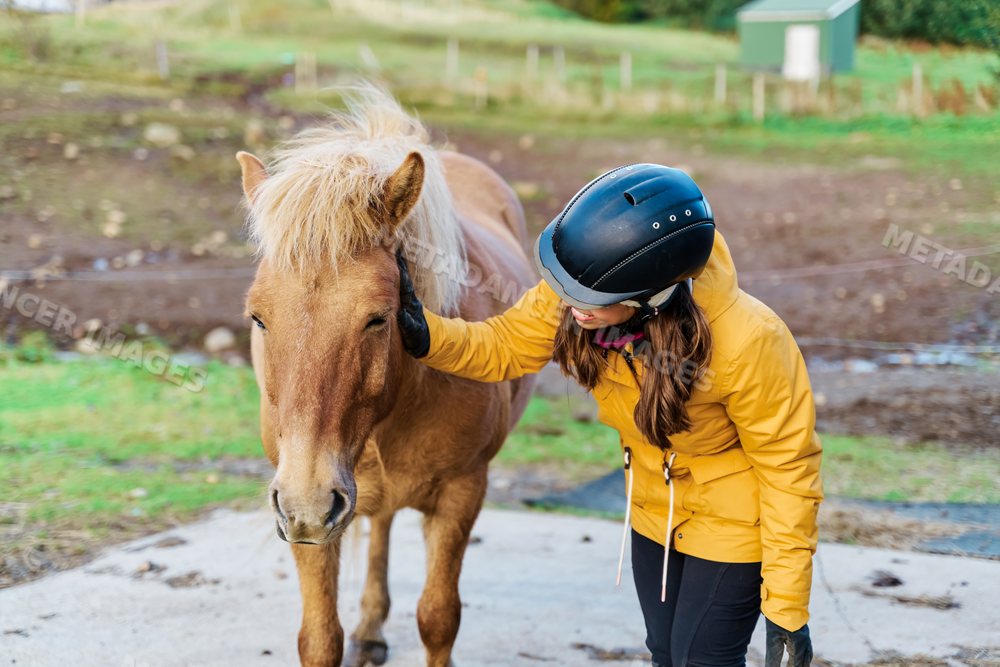 A white woman gently pets a horse outdoors