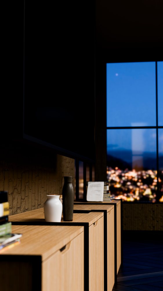 Vases and books decorate a wooden cabinet inside a modern room at night with a city light view through the window.