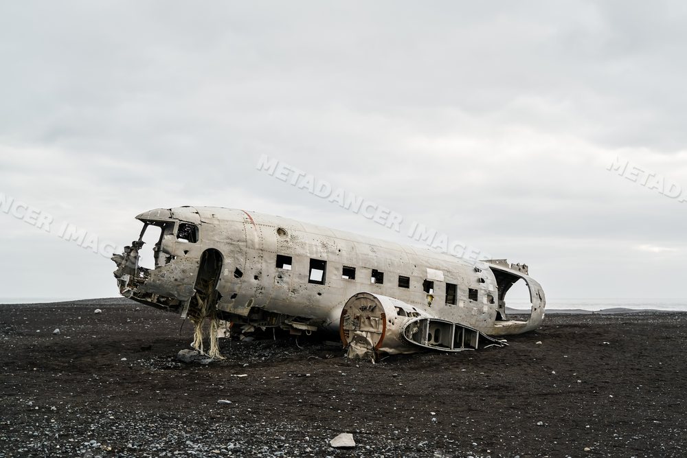 Old airplane wreckage lies on a black sand beach in a beach