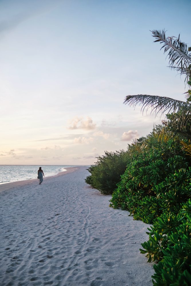 A woman walking along a peaceful sandy beach at sunset in the Maldives