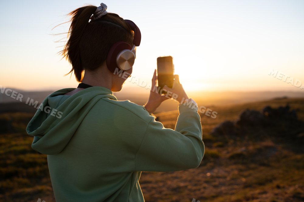 White Woman takes a photo of a sunset landscape outdoors