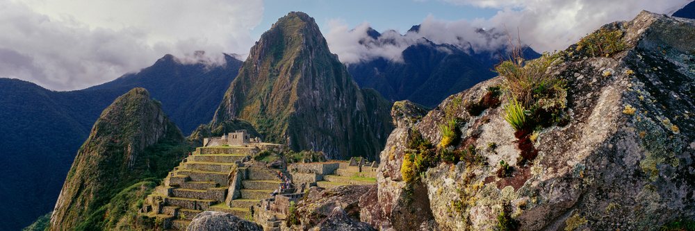 Stone terraces and ancient buildings of Machu Picchu with mountain peaks and cloudy sky in Peru.