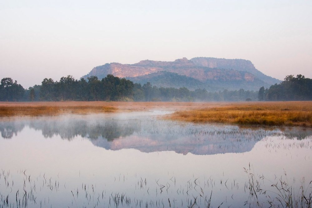 Misty morning landscape of Bandhavgarh National Park with forested hills and water reflecting the trees, Madhya Pradesh, India.
