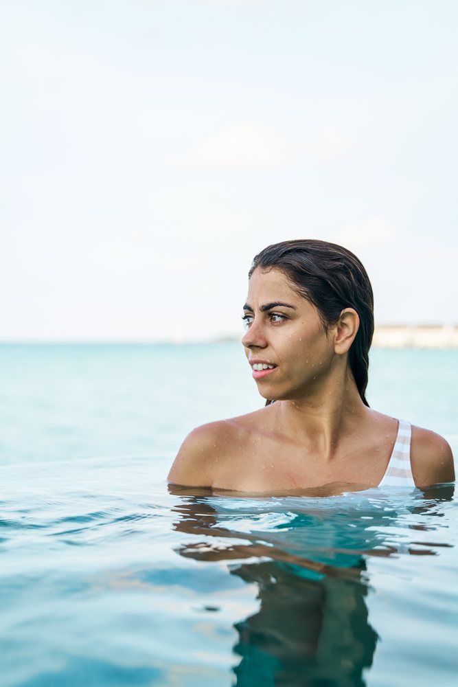 A white woman in a swimsuit stands in clear pool water