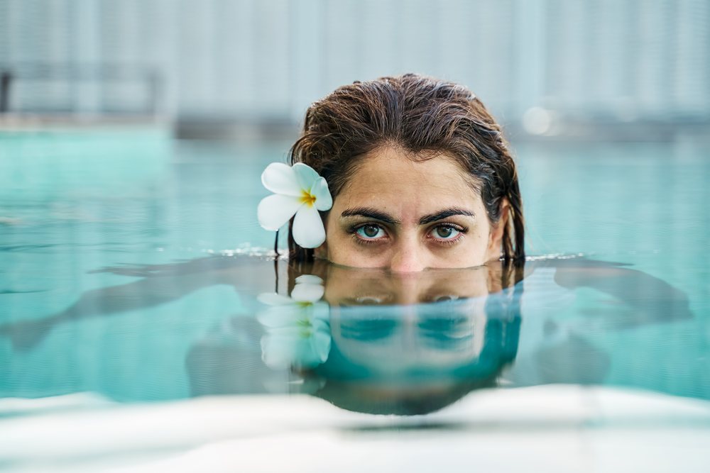 A white woman swims partially submerged in a calm blue pool