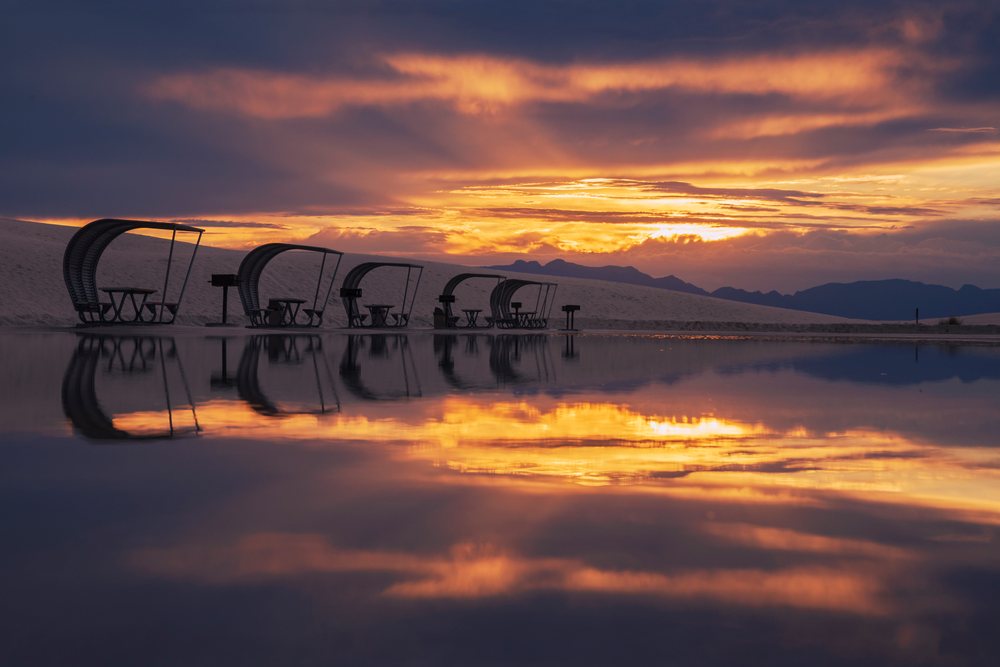 Picnic shelters reflect on calm water at sunset amidst white sand dunes in white Sands National Monument desert, Landscape, Wildlife, Alamogordo, New Mexico, USA.