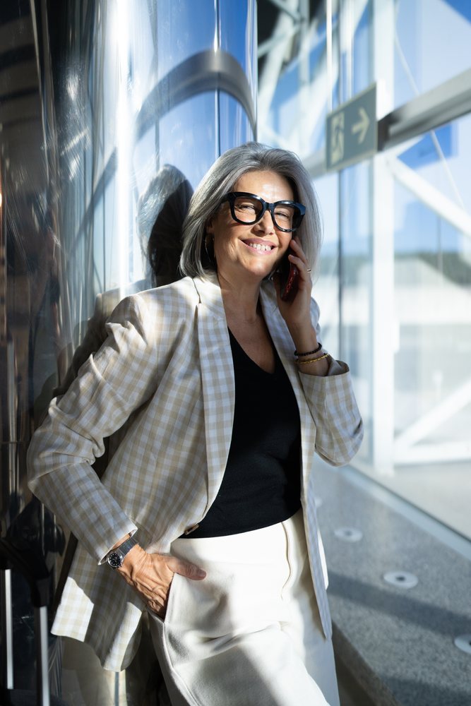 Businesswoman with gray hair smiling while talking on a mobile phone inside a modern building, Spain, Madrid.