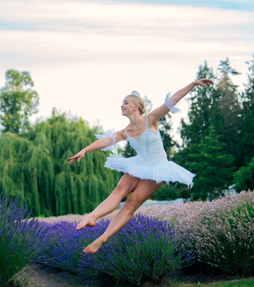 A ballerina in a white tutu leaps gracefully over a lavender field on a summer day, WA, USA.