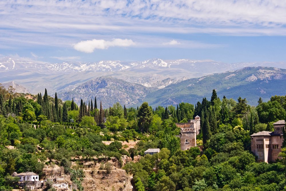 Sierra Nevada mountain range with forested hills and historic castle towers, Spain under a blue sky with clouds, Andalucia.
