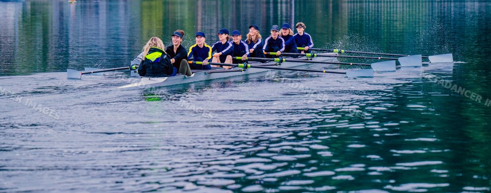 A white women's rowing team practices together on a calm lake
