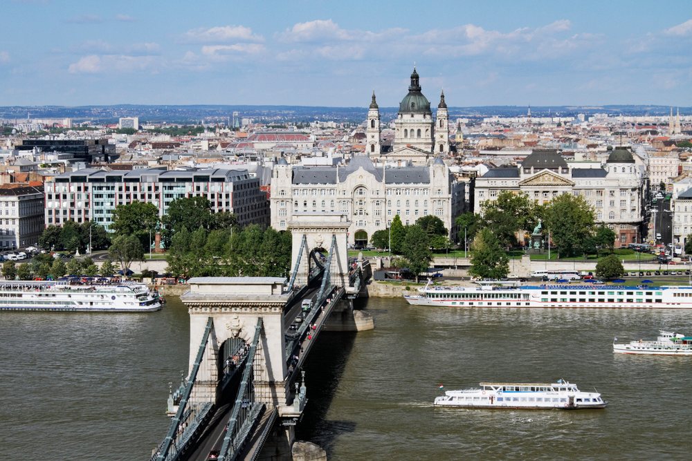 Chain Bridge spans the River Danube with boats on the water and the Budapest cityscape in the background, Hungary.