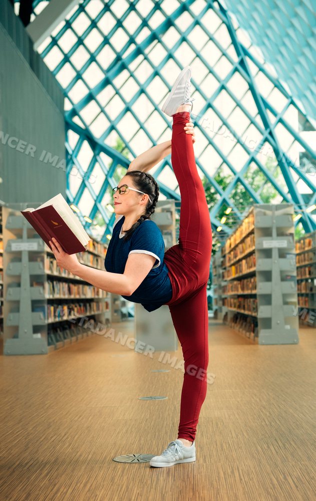 A young woman does a yoga stretch while reading a book