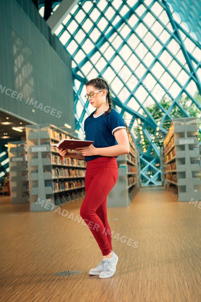Teenage girl reading a book standing in a library