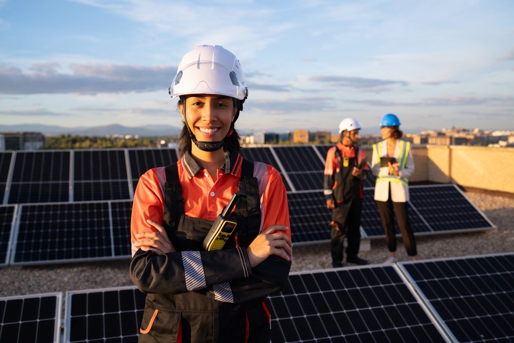 Woman worker wearing a safety helmet and communication radio stands outdoors at a solar energy site with solar panels, Madrid, Spain.