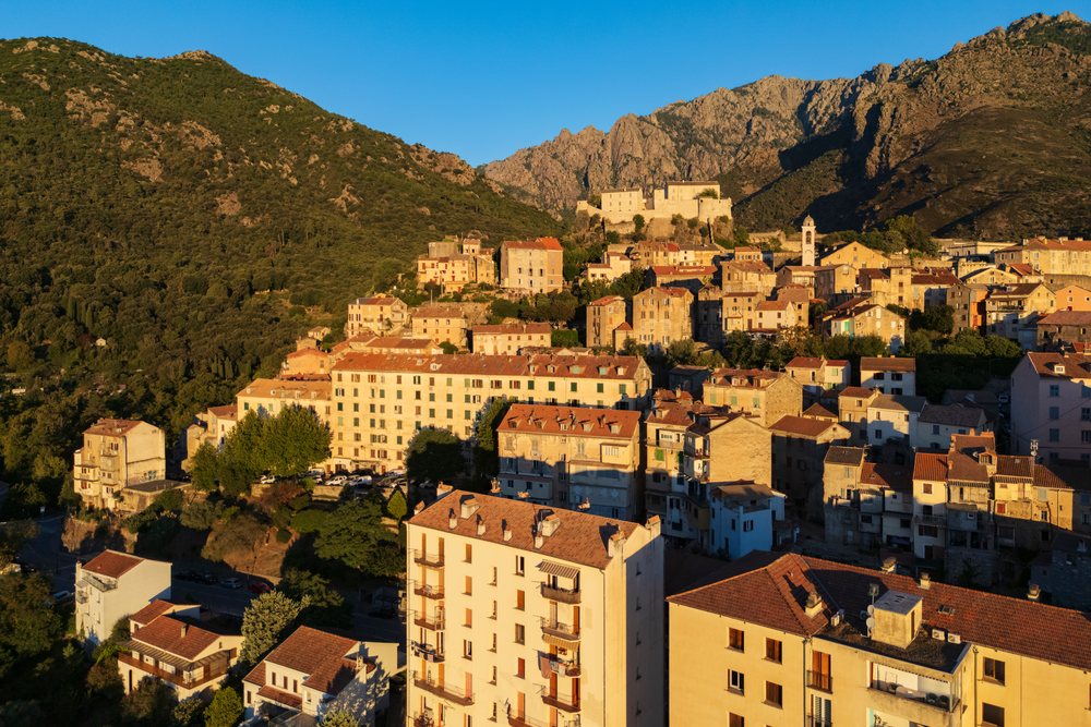 Early morning light over the town of Corté, showing historic buildings and surrounding mountains under a clear sky, Travel Photography, Corsica, France.