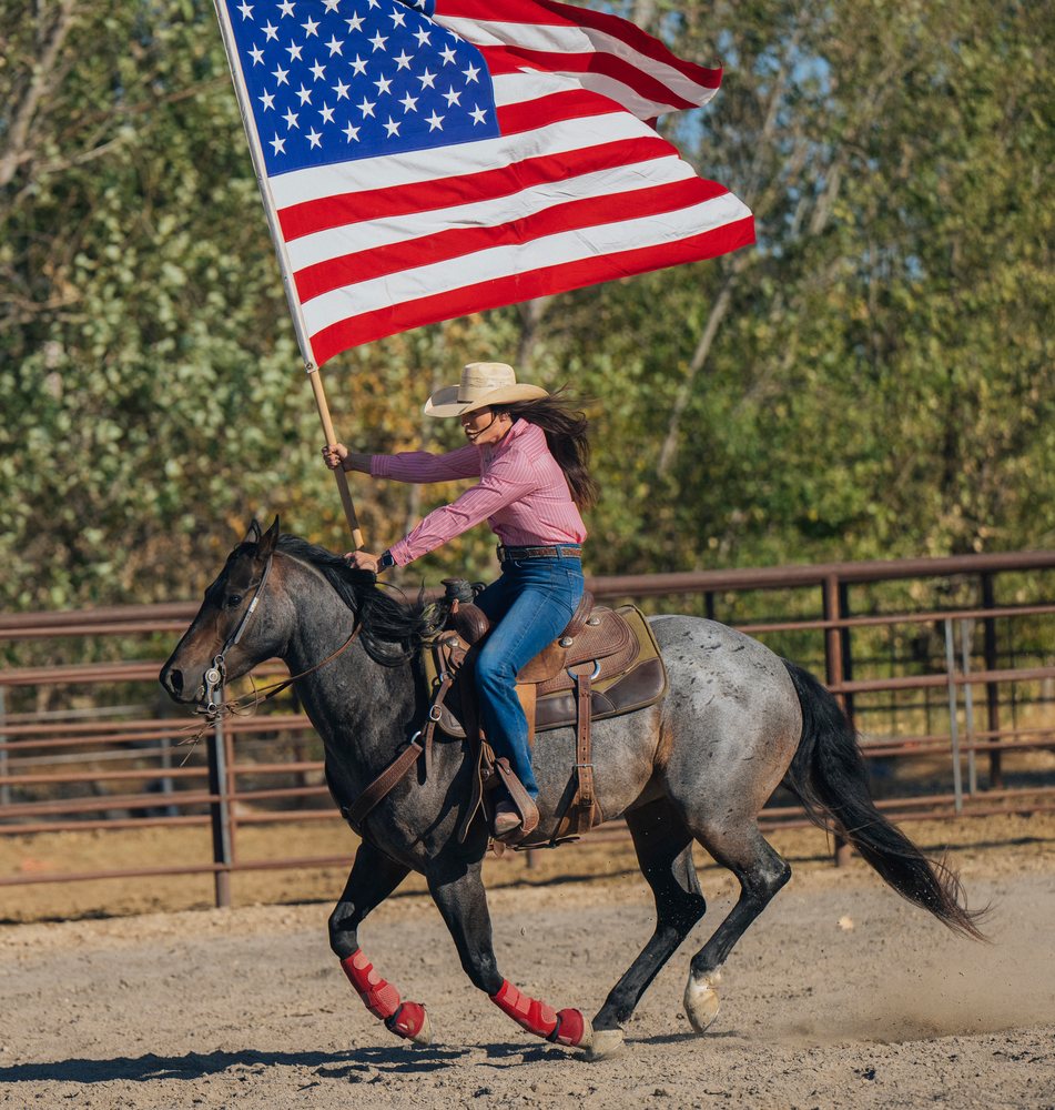 Cowgirl riding a running horse waving an American flag in an outdoor rodeo arena, Southwest USA.