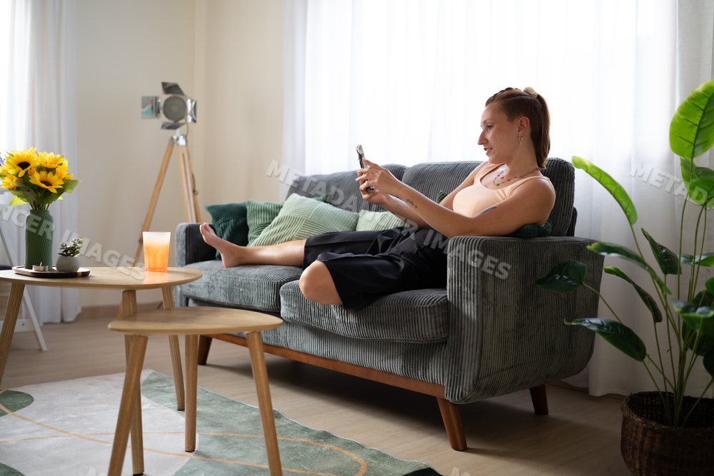 A white woman sits on a sofa using her smartphone