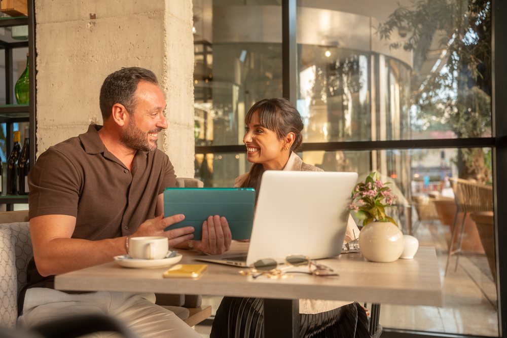 Two coworkers engage in a business discussion using a laptop and tablet at a cafe table, Seville, Andalucia.