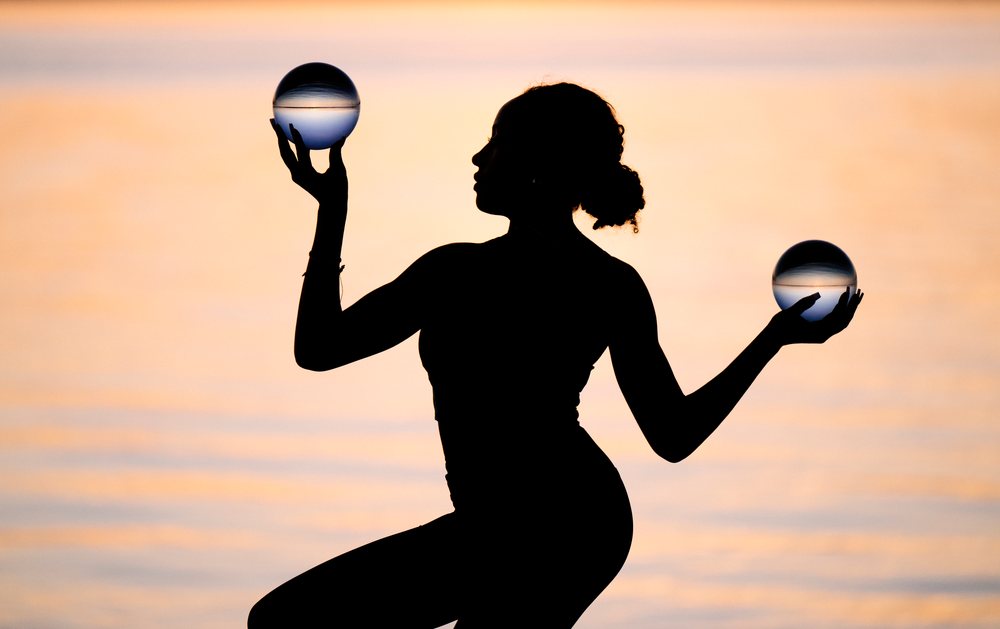 Silhouette of a woman practicing yoga and acrobatics with glass balls at sunset over water, USA.