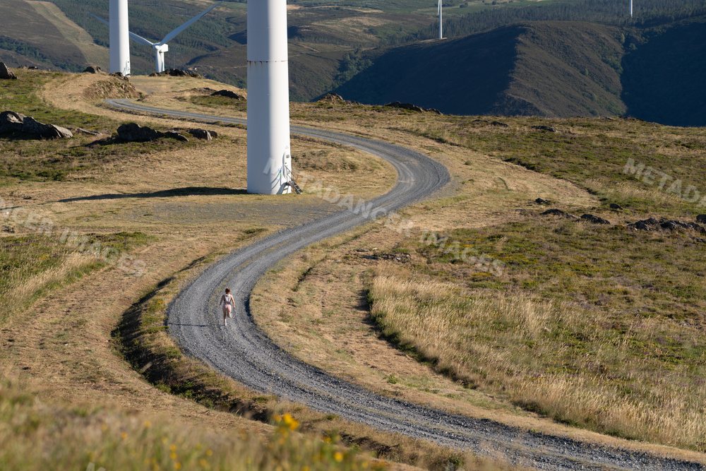 White Woman running on gravel road by wind turbines in Galicia Spain