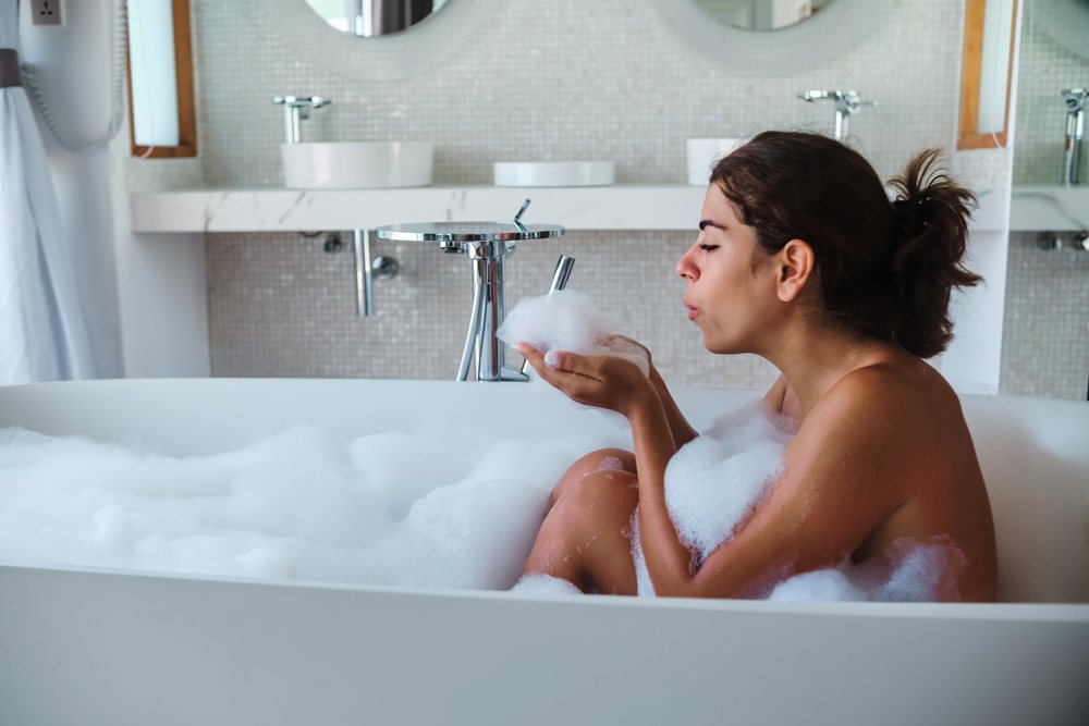 A woman enjoys a relaxing bubble bath while blowing foam from her hands in a modern bathroom in the, Maldives.