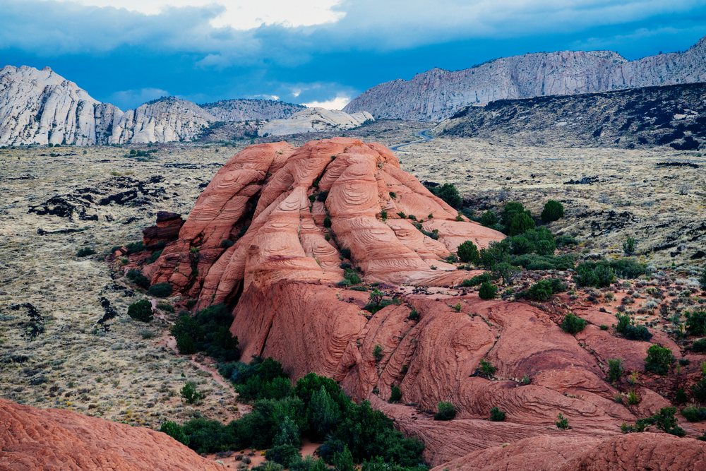 Red rock formation with green shrubs in arid desert landscape of State Park, USA under a cloudy sky, Snow Canyon, red Cliffs Desert, Utah.