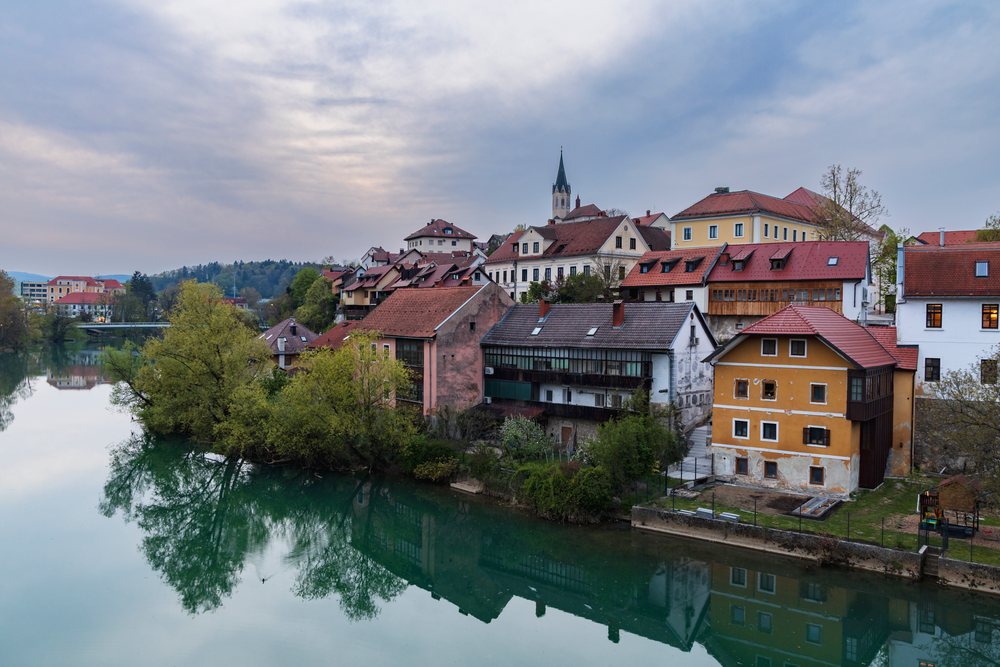 River Krka flows beside houses and trees reflecting at Dusk, landscape, cityscape, Novo Mesto, Slovenia.