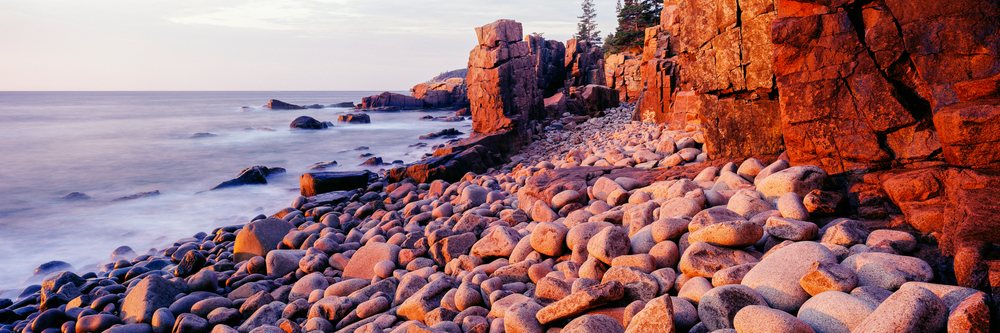 Sunset over a rocky coastline with boulders, cliffs, and calm ocean waters at Acadia National Park, Maine, Acadia National Park Maine, USA.