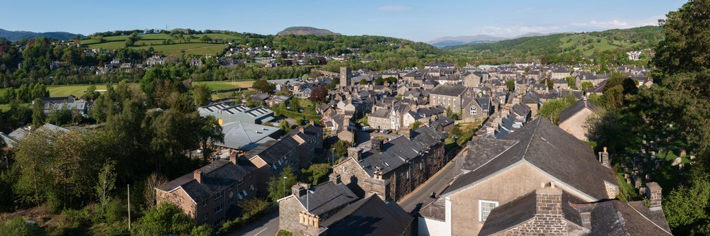 Aerial view of Dolgellau town showing houses, stone roofs, church tower, surrounding hills, mountains, and abundant greenery under clear sky, Landscape, Gwynedd, Wales.