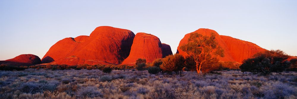 Sunlight illuminates the red rock formations of The Olgas, Northern Territory, Australia.