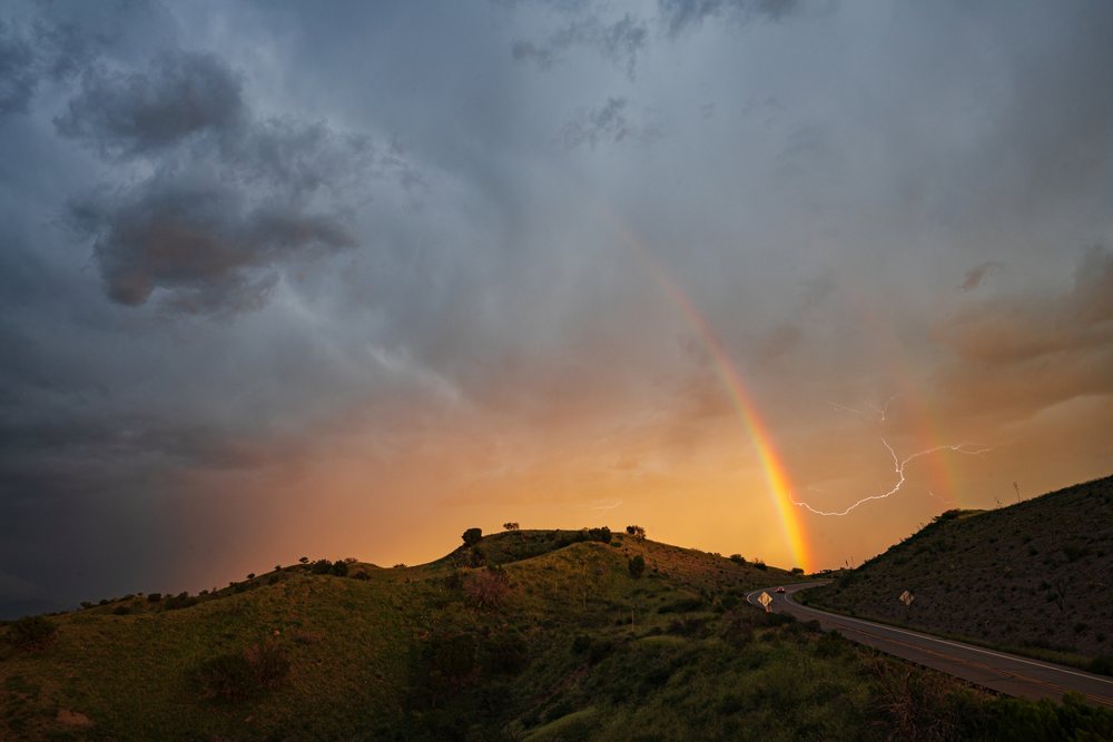 Rainbow and lightning bolt visible over hilly terrain with greenery at sunset on Arizona Highway 83 near Helvetia Lookout, Storm Chasing, Weather, Environmental Issues, Sonoita, USA.