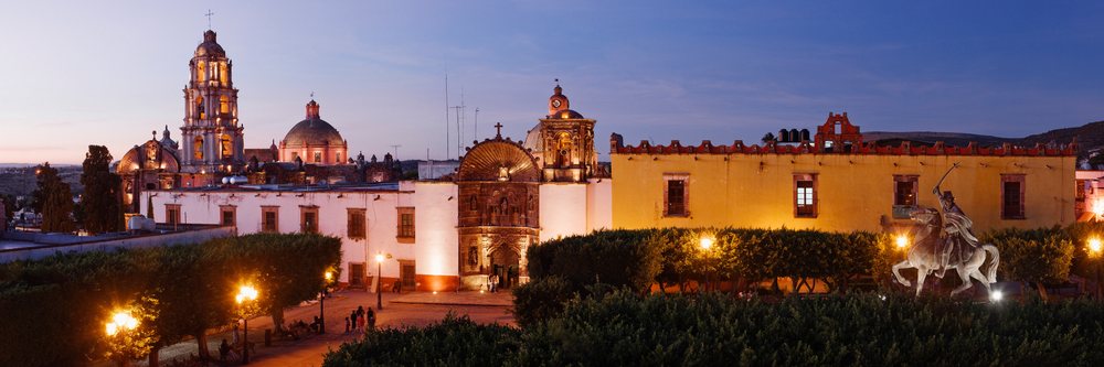 The Plaza de la Republica square, features an illuminated historic church and equestrian statue at twilight, San Miguel de Allende, Mexico.