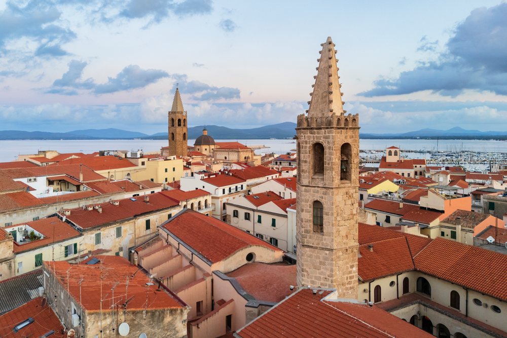 The Monastery of San Francesco and Cathedral towers overlook red-tiled rooftops and the Mediterranean Sea at Dawn, Travel Images, Alghero, Sardinia, Italy.