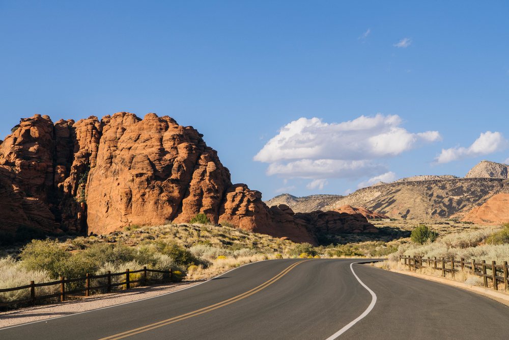 Curved paved road passing red cliff rock formations and desert scrub under a clear blue sky at red Cliffs Desert State Park, Snow Canyon, Utah, USA.