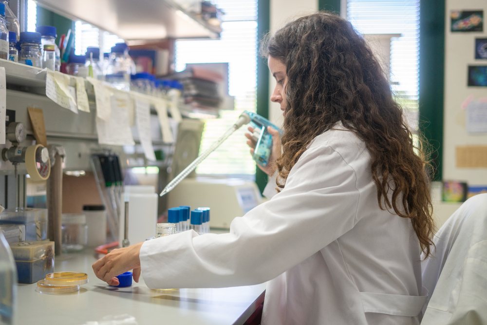 Female scientist in a white lab coat using a pipette with petri dishes at a laboratory bench, research, biology, Seville, Andalucía.