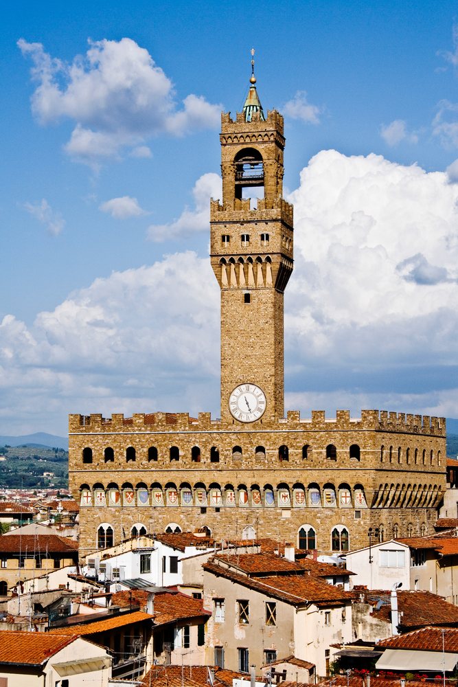 Palazzo Vecchio's medieval clock tower rises above rooftops under a clear blue sky, Florence, Italy.