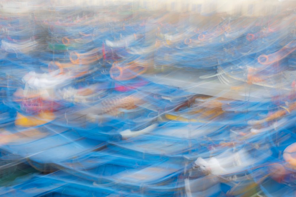 Multiple blue Fishing Boats docked closely at the harbor, with visible fishing nets and orange life rings, captured using intentional camera movement creating motion blur, Landscape, Lifestyle, Essaouira, Province, Morocco.