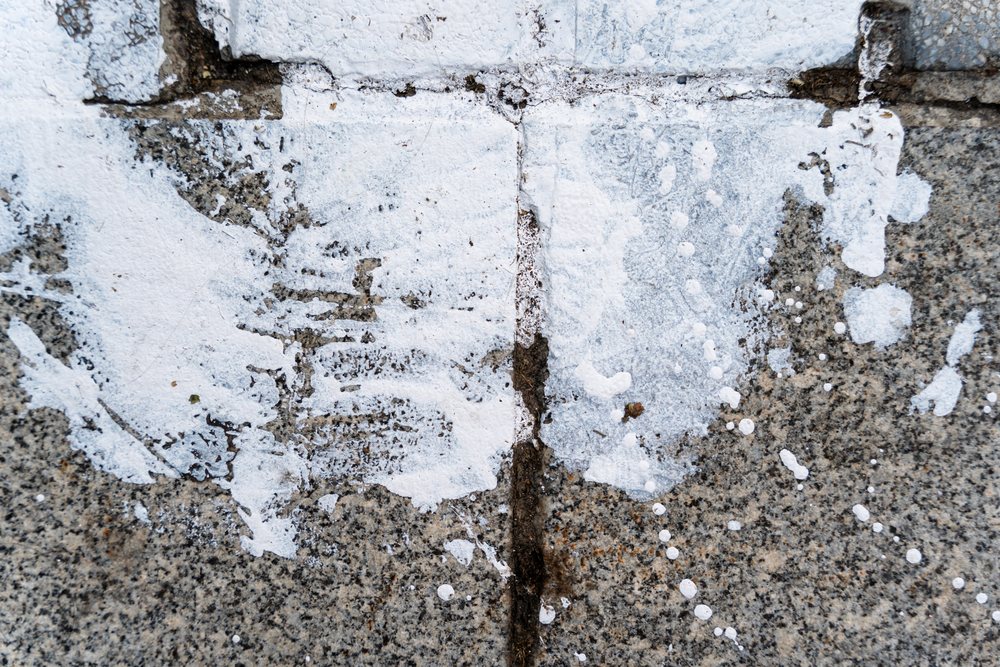 White paint splatter and footprint on cracked concrete sidewalk in an outdoor urban setting, texture, abstract texture, background, wallpaper, Spain.