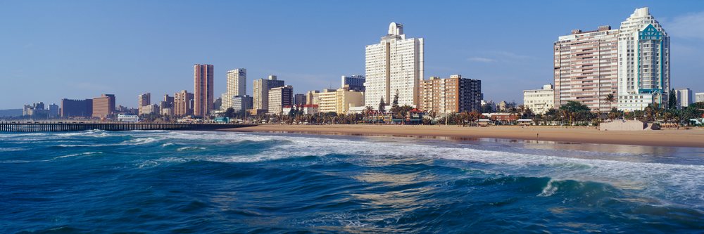 Cityscape showing high-rise buildings along a beach with waves under a clear blue sky.