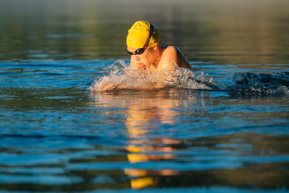 Swimmer wearing a yellow swim cap and goggles performing a breaststroke in open water, USA.