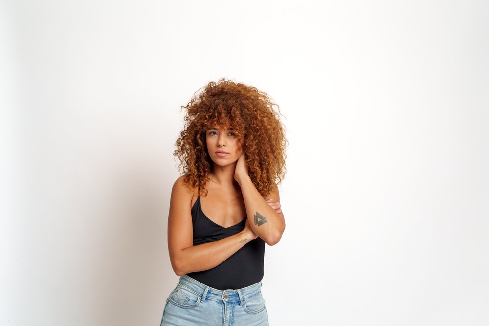 Woman with curly red hair and tattoo on left forearm standing and posing in a studio against a white background, Malaga, Spain.