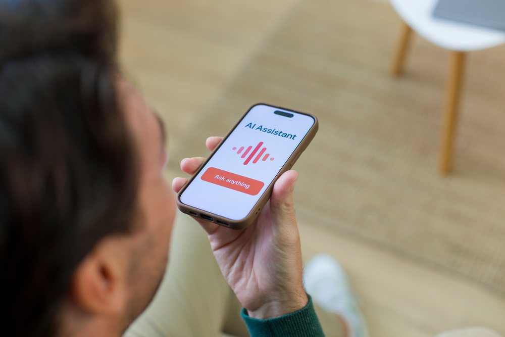 Person sitting indoors at home holding a smartphone displaying an AI assistant app interface, Young adult.