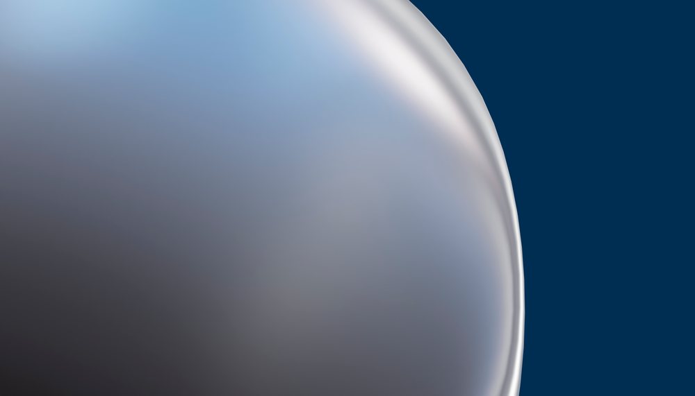 Close-up of a shiny soap bubble with iridescent colors and smooth surface against a blue background.