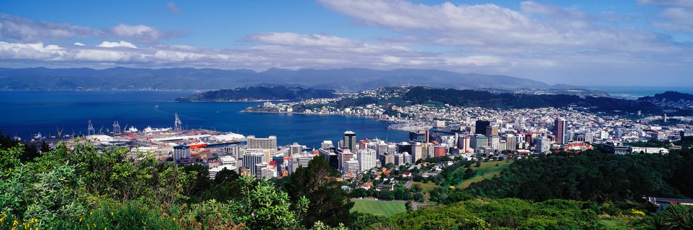 Panoramic view of Wellington cityscape and harbor with hills and partly cloudy sky, New Zealand.