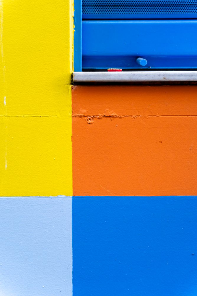 Colorful painted wall with yellow, orange, blue, and light blue sections and a closed blue window shutter, texture, abstract texture, background, wallpaper, Spain.