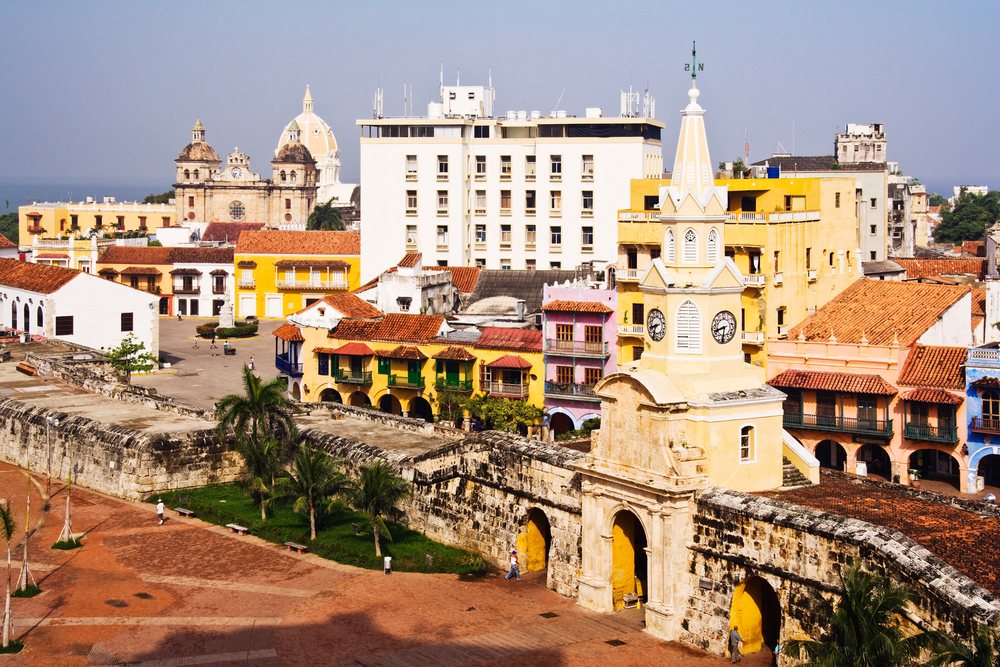 Historic clock tower with weather vane and colonial buildings along a fortified wall's Plaza de los Coches, Cartagena, Colombia.